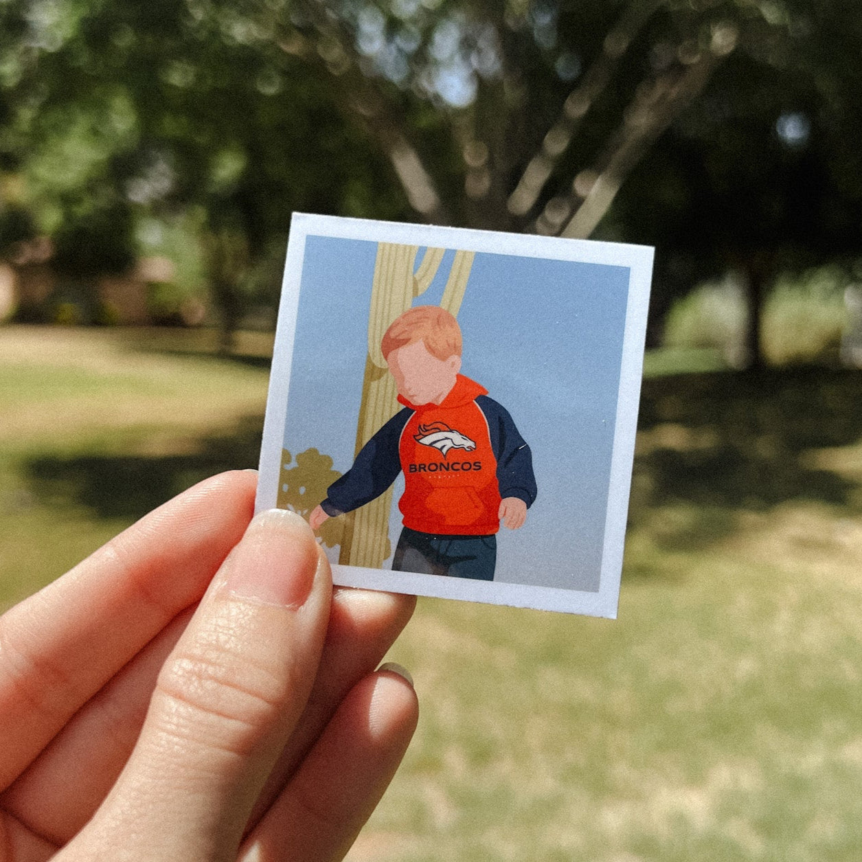 Hand holding custom illustrated Polaroid magnet of a little boy in Broncos hoodie — sports-themed kids keepsake